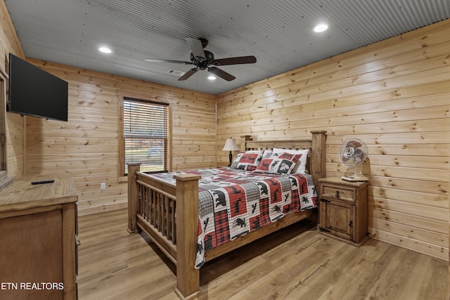 bedroom featuring light hardwood / wood-style flooring, ceiling fan, and wooden walls