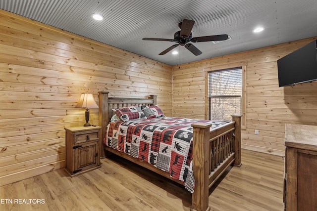 bedroom with light hardwood / wood-style floors, ceiling fan, and wooden walls