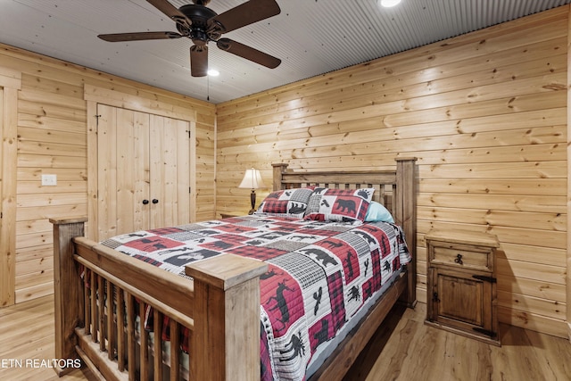 bedroom featuring hardwood / wood-style flooring, ceiling fan, and wooden walls