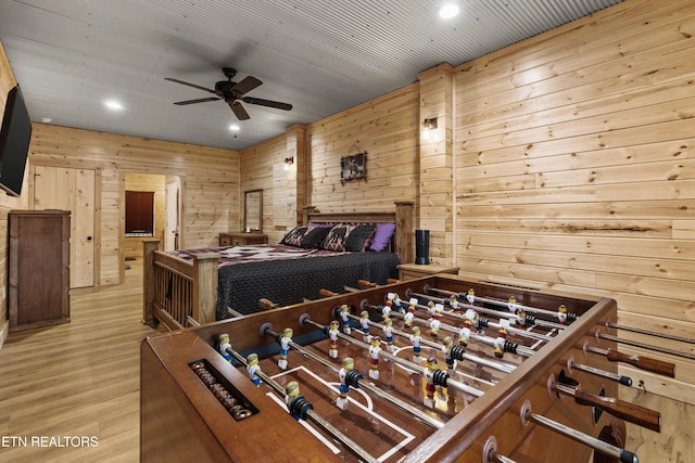 bedroom featuring light hardwood / wood-style flooring, ceiling fan, and wooden walls