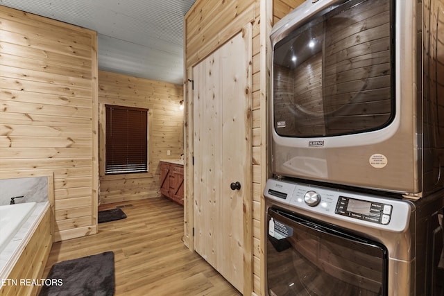 clothes washing area with stacked washer and dryer, wooden walls, and light hardwood / wood-style floors