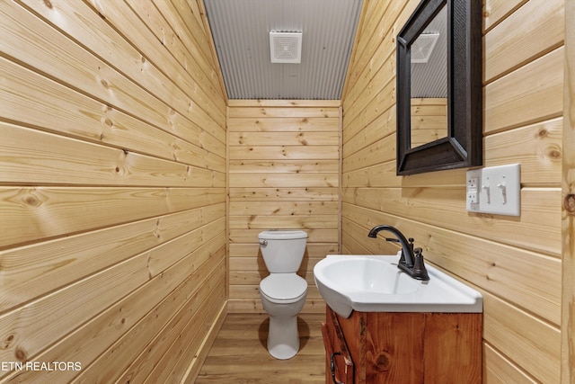 bathroom with vanity, toilet, wood-type flooring, and wooden walls