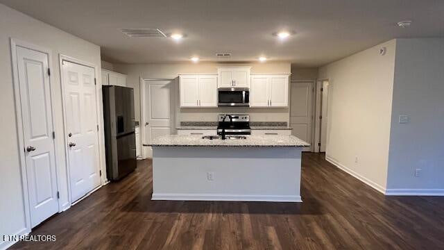 kitchen featuring light stone countertops, stainless steel appliances, dark hardwood / wood-style floors, an island with sink, and white cabinets