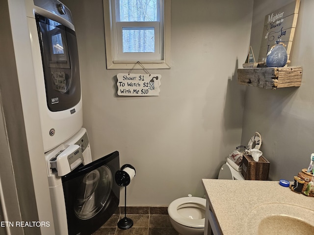 bathroom featuring tile patterned floors, vanity, stacked washing maching and dryer, and toilet