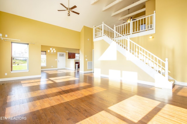 unfurnished living room with ceiling fan with notable chandelier, wood-type flooring, a towering ceiling, and beam ceiling