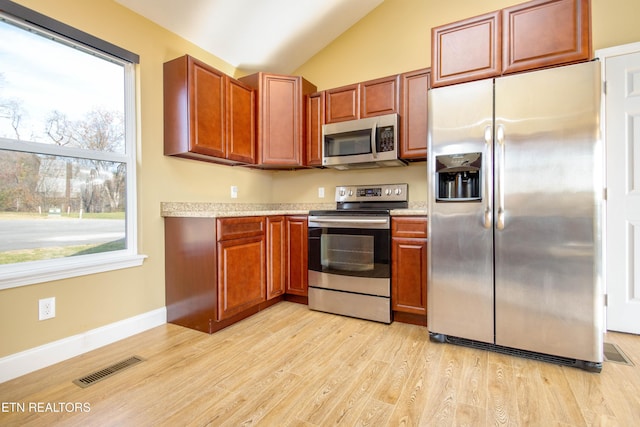 kitchen with appliances with stainless steel finishes, light hardwood / wood-style floors, vaulted ceiling, and a wealth of natural light