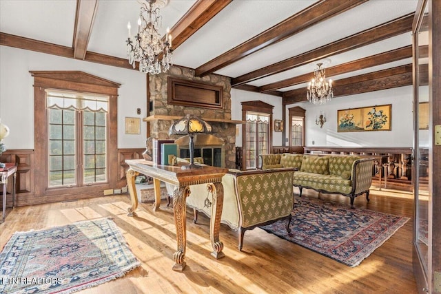 living room with wood-type flooring, an inviting chandelier, a stone fireplace, and beam ceiling