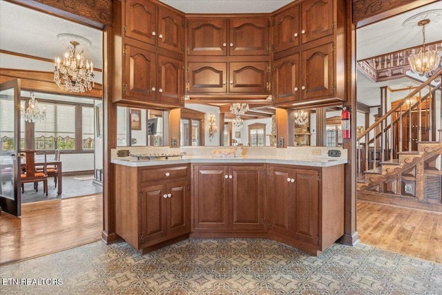 kitchen featuring kitchen peninsula, ornamental molding, pendant lighting, light hardwood / wood-style flooring, and a chandelier