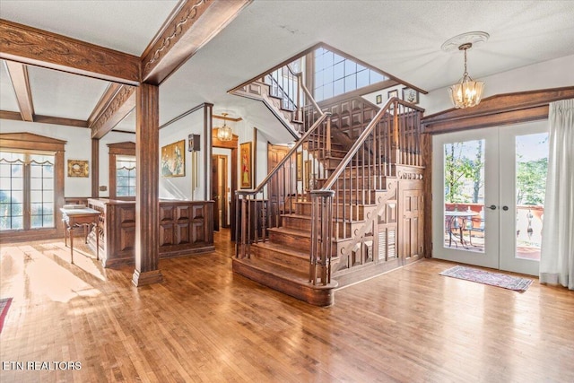 entrance foyer featuring french doors, hardwood / wood-style flooring, a textured ceiling, beam ceiling, and a chandelier