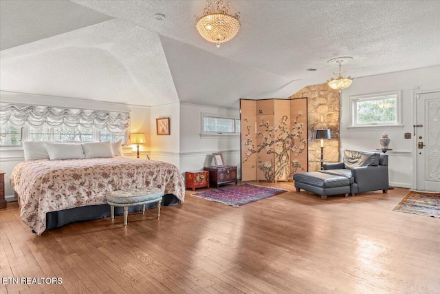 bedroom with a textured ceiling, wood-type flooring, vaulted ceiling, and a notable chandelier