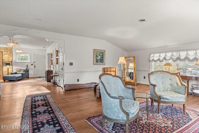 living area with a textured ceiling, wood-type flooring, and lofted ceiling