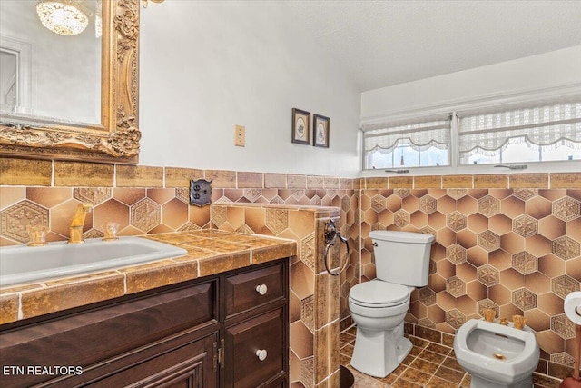 bathroom featuring a bidet, a textured ceiling, toilet, vanity, and tile walls