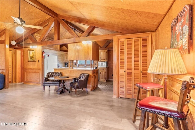 kitchen with wood walls, lofted ceiling with beams, white appliances, and light wood-type flooring