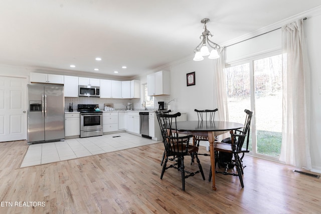 dining space with light wood-type flooring, an inviting chandelier, and ornamental molding