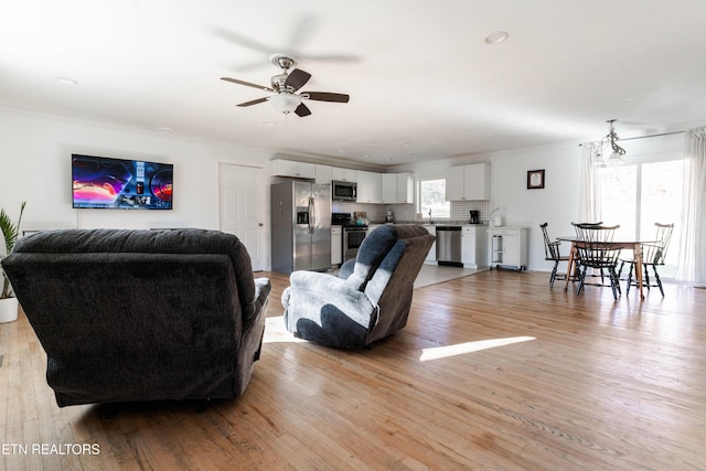 living room with ceiling fan with notable chandelier, light hardwood / wood-style floors, and crown molding