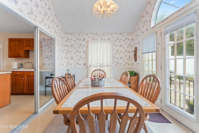 dining space with a healthy amount of sunlight, light colored carpet, lofted ceiling, and an inviting chandelier