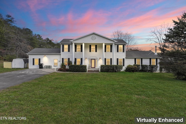 neoclassical home featuring a lawn and a storage shed