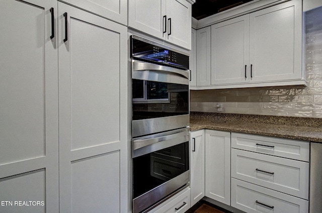 kitchen featuring decorative backsplash, double oven, white cabinetry, and dark stone countertops