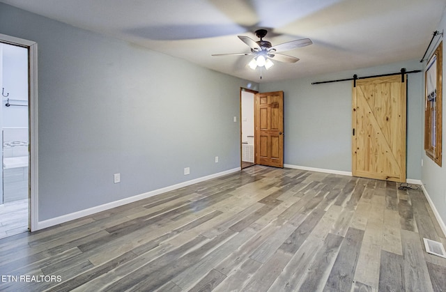 unfurnished bedroom with ceiling fan, connected bathroom, a barn door, and hardwood / wood-style flooring