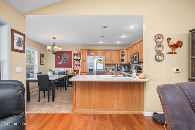 kitchen with decorative backsplash, light hardwood / wood-style floors, kitchen peninsula, stainless steel appliances, and a chandelier