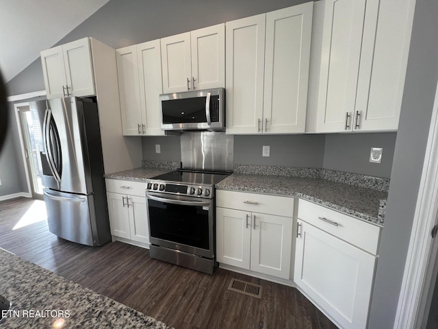 kitchen with lofted ceiling, appliances with stainless steel finishes, white cabinetry, dark hardwood / wood-style floors, and stone countertops