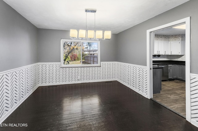 unfurnished dining area featuring breakfast area, dark hardwood / wood-style floors, an inviting chandelier, and tile walls