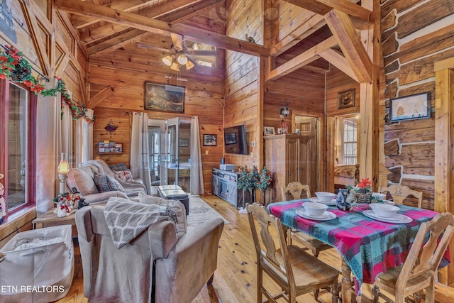 dining room with ceiling fan, light hardwood / wood-style flooring, high vaulted ceiling, beamed ceiling, and wood walls