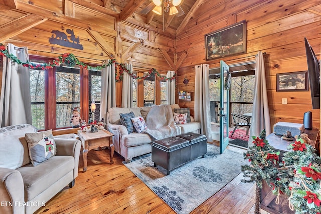 living room featuring hardwood / wood-style floors, ceiling fan, wood walls, and vaulted ceiling with beams