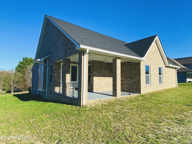 rear view of property featuring a yard, brick siding, and roof with shingles