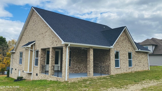 back of house with brick siding, a lawn, and roof with shingles