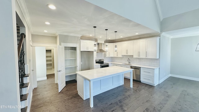 kitchen with dark wood finished floors, wall chimney exhaust hood, ornamental molding, stainless steel appliances, and a sink