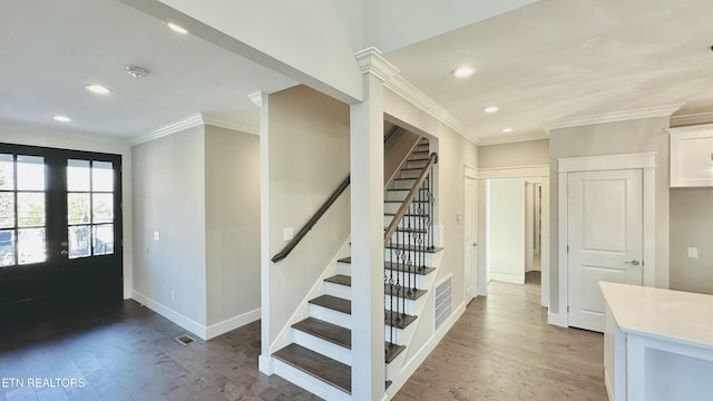 foyer with wood finished floors, visible vents, baseboards, ornamental molding, and stairway