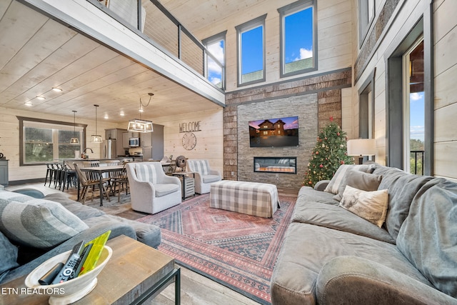 living room with a stone fireplace, wood walls, wooden ceiling, and a high ceiling