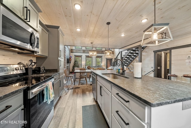 kitchen featuring sink, an island with sink, decorative light fixtures, appliances with stainless steel finishes, and hardwood / wood-style flooring