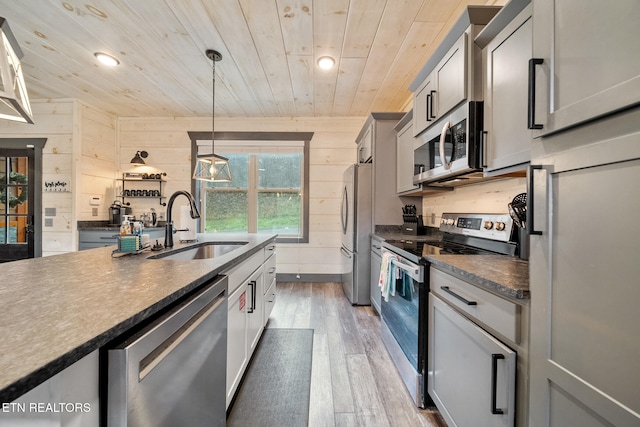 kitchen featuring hanging light fixtures, wooden walls, sink, appliances with stainless steel finishes, and wood-type flooring