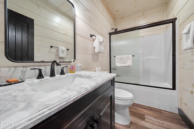 full bathroom featuring vanity, hardwood / wood-style flooring, wooden walls, and bath / shower combo with glass door