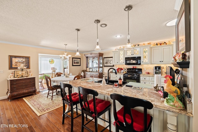 kitchen with dark wood-type flooring, black appliances, sink, crown molding, and decorative light fixtures