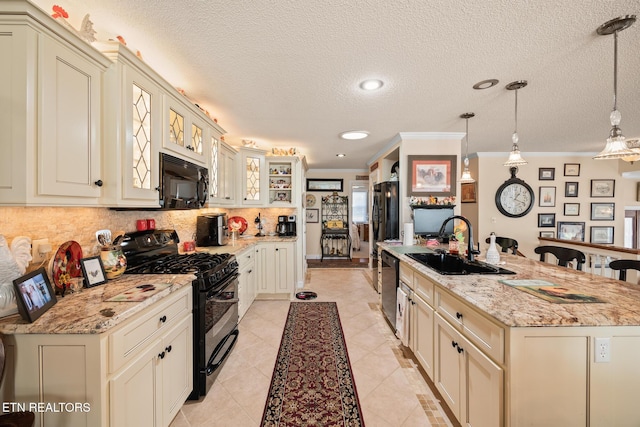 kitchen featuring sink, pendant lighting, cream cabinetry, a center island with sink, and black appliances