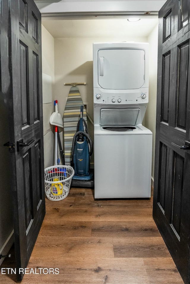 clothes washing area with dark wood-style floors, laundry area, and stacked washer / drying machine