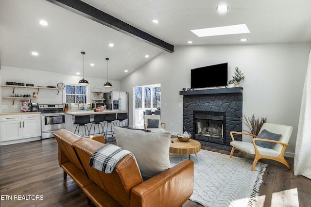 living area with vaulted ceiling with skylight, dark wood finished floors, a stone fireplace, and recessed lighting