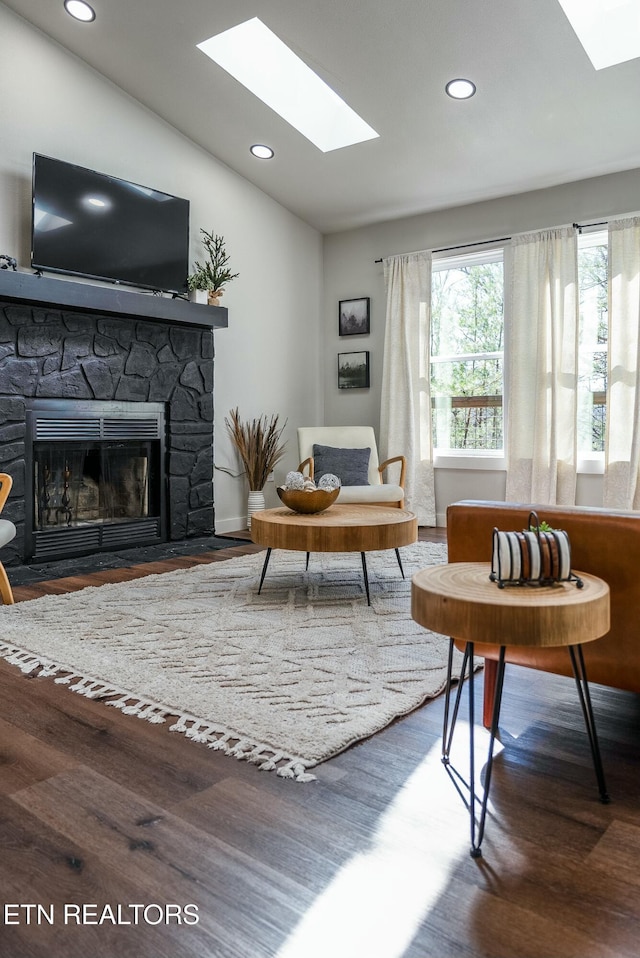 interior space with vaulted ceiling, a stone fireplace, wood finished floors, and recessed lighting