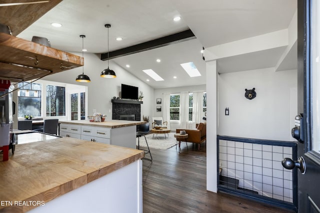 kitchen featuring vaulted ceiling with skylight, open floor plan, dark wood-type flooring, white cabinetry, and pendant lighting