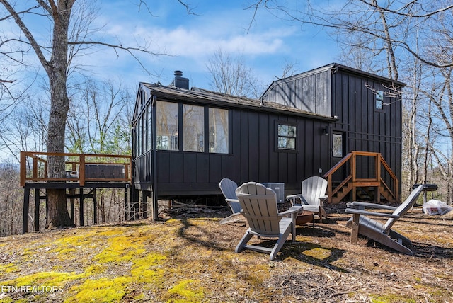 rear view of property with a fire pit, a shingled roof, board and batten siding, and a chimney