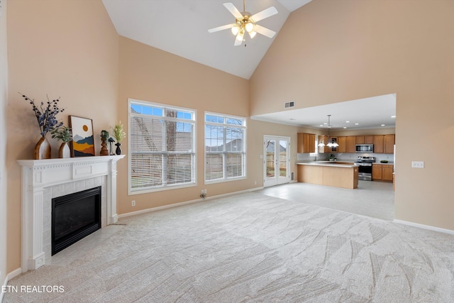 unfurnished living room featuring a tiled fireplace, high vaulted ceiling, light colored carpet, and ceiling fan