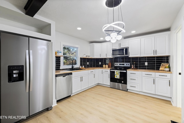 kitchen with pendant lighting, white cabinets, appliances with stainless steel finishes, butcher block countertops, and light hardwood / wood-style floors