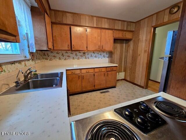 kitchen with brown cabinets, light countertops, stove, freestanding refrigerator, and a sink