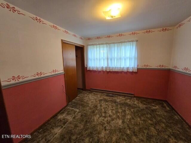 carpeted spare room with a baseboard heating unit and wainscoting