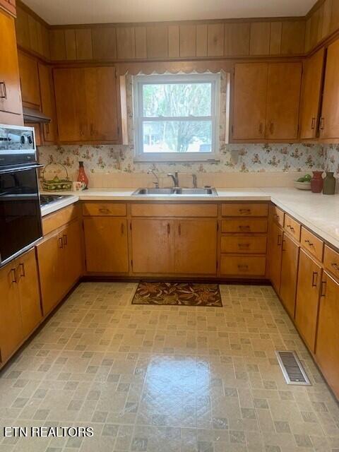 kitchen featuring light countertops, visible vents, brown cabinetry, a sink, and oven