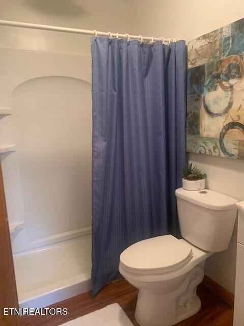 full bathroom with toilet, curtained shower, baseboards, and wood finished floors