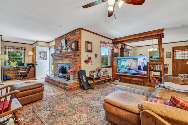 living room featuring ceiling fan with notable chandelier, a fireplace, wood-type flooring, and ornamental molding